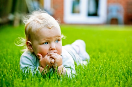 Bébé dans l'herbe qui se mange les doigts avant d'aller chez l'ostéopathe