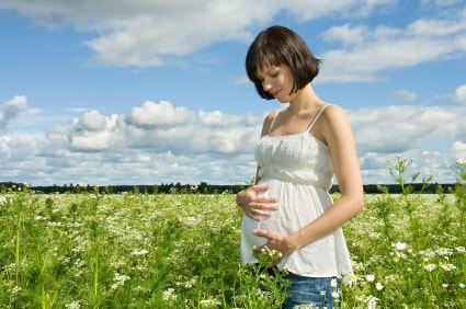 Femme enceinte dans un champ de fleur qui regarde son ventre heureuse d'aller chez l'ostéopathe