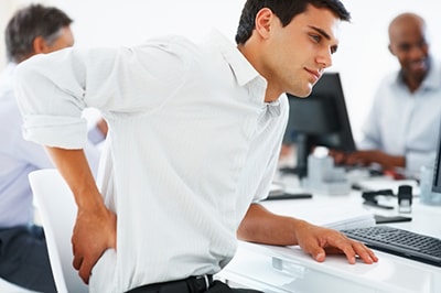 Homme assis à son bureau qui se tient le dos qui parait avoir mal